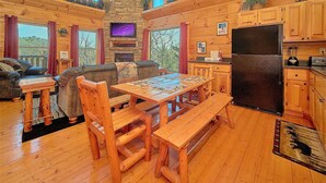 A cozy cabin interior with a wooden dining table, benches, a fireplace, and a kitchen area with cabinets and a refrigerator. - Aug Special-Secluded, Privacy, Mountain View, Sunset, 3D Movies, Hot Tub,Game Rm (Sevierville)
