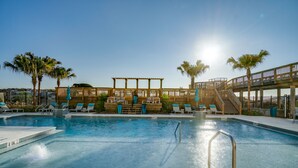 Una piscina con muelle de madera, sillas de descanso y palmeras.