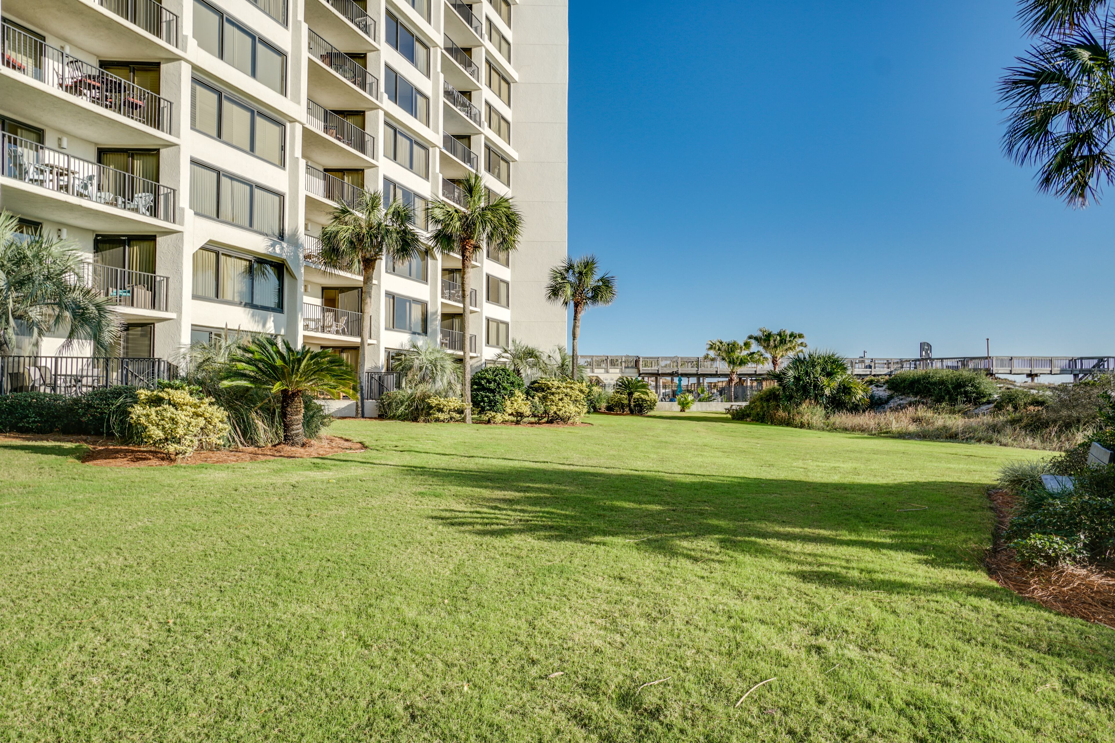 A multi-story hotel with balconies, a well-maintained lawn, and palm trees.