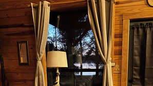 Ein gemütliches Blockhaus-Interieur mit Schaukelstuhl, Lampe, kleinem Tisch und einem Fenster mit Vorhängen.