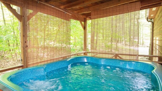 A hot tub in a covered wooden structure with a view of a forested area.