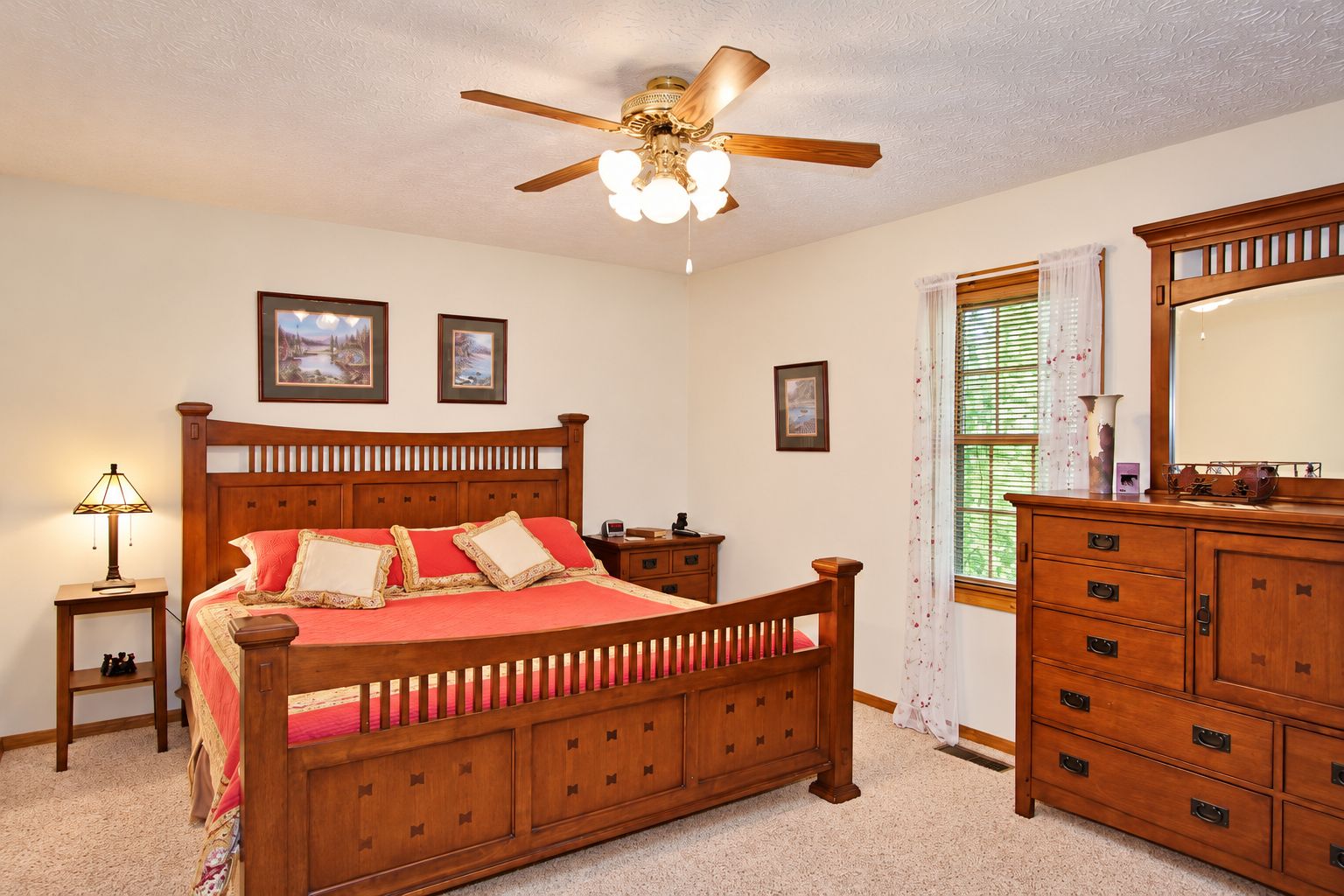 A bedroom with a wooden bed, a nightstand, a dresser, a ceiling fan, and framed pictures on the wall.