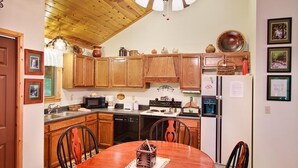A kitchen with wooden cabinets, a dining table with chairs, and a refrigerator.