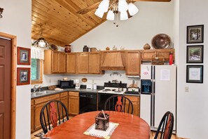 A kitchen with wooden cabinets, a dining table with chairs, a microwave, a coffee maker, and a refrigerator.