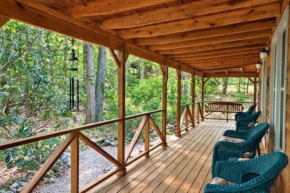 A covered wooden deck with a railing, surrounded by lush greenery and trees.