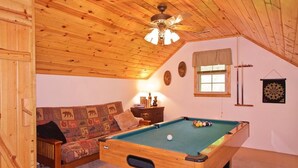 A cozy room with a pool table, a sofa with a quilted cover, a ceiling fan, and a dartboard on the wall.