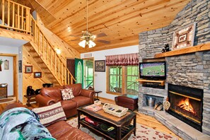 A cozy living room with a stone fireplace, wooden ceiling, and a staircase.