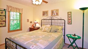 A bedroom with a bed, a ceiling fan, a window with blinds, and a bedside table with a lamp.