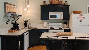 A kitchen with black cabinets, a white countertop, a microwave, a stove, and a refrigerator. There are two pendant lights hanging above the counter. - Hawk's Nest Hideaway With Creek That Runs Through This Very Private Property (Mentone)