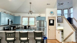 Une cuisine avec des meubles de couleur bleue, un îlot central doté de tabourets, un réfrigérateur et un ventilateur de plafond.