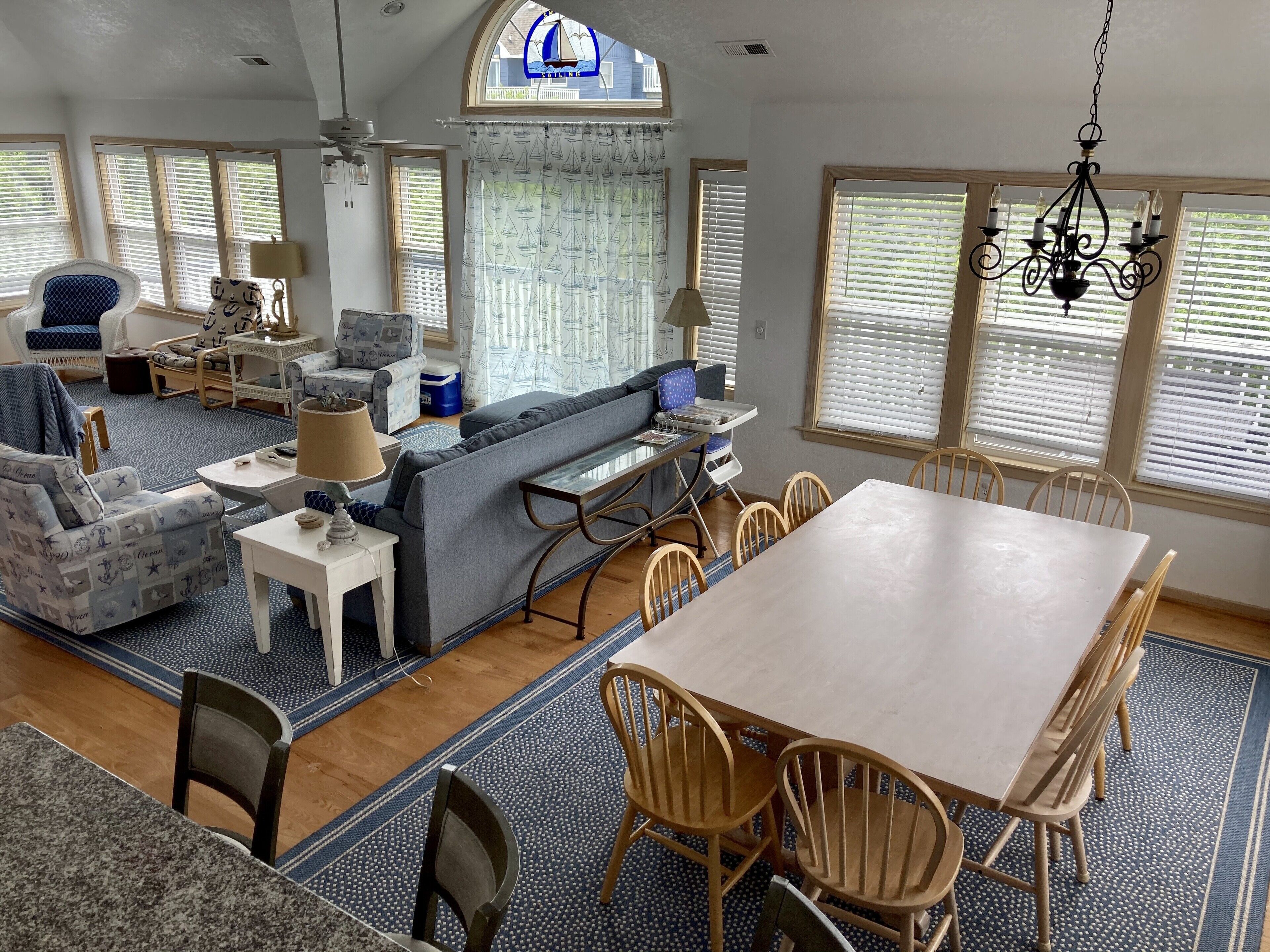 A spacious living room with a large dining table, comfortable seating, and large windows with blinds.