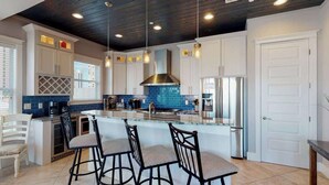 A modern kitchen with white cabinets, a blue backsplash, a stainless steel range hood, and a central island with bar stools.