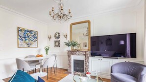 Uma sala de estar com lareira, um espaço de refeições com mesa branca e uma televisão grande.
