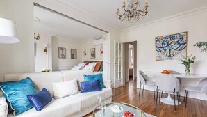 Uma sala de estar moderna com um sofá branco, almofadas azuis e brancas, uma mesa de centro redonda de vidro e um candelabro.