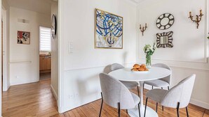 Uma área de refeições com uma mesa redonda, quatro cadeiras cinzentas e um vaso com flores.