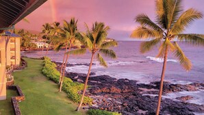 A coastal hotel with a view of the ocean, palm trees, and a rainbow.