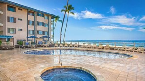 A hotel with a pool area featuring two hot tubs, lounge chairs, and a view of the ocean.
