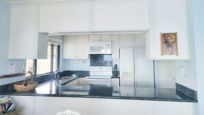 A modern kitchen with white cabinets, a granite countertop, a microwave, a stove, and a refrigerator.