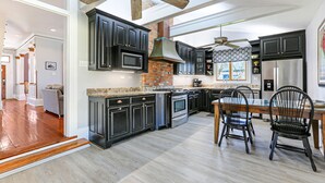 Una cocina moderna con muebles oscuros, una chimenea de ladrillo y un comedor con sillas negras.