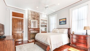 Un dormitorio con chimenea de ladrillo, una cama grande, un aparador y un ventilador de techo.