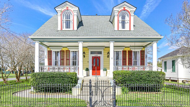 Una casa de dos pisos con puerta roja, columnas blancas y un balcón.