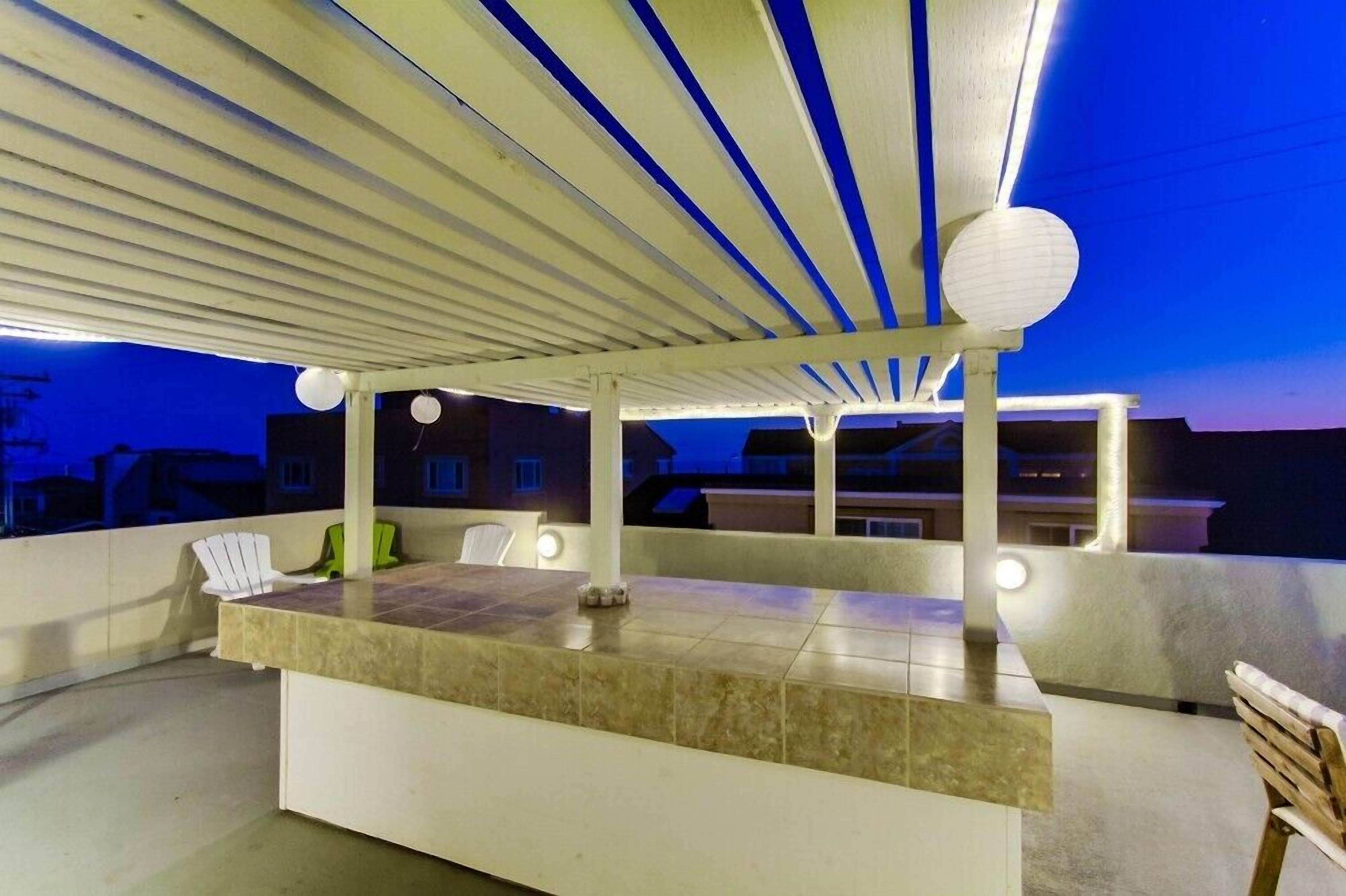 An outdoor bar area with a tiled countertop, seating, and a ceiling with a light fixture.