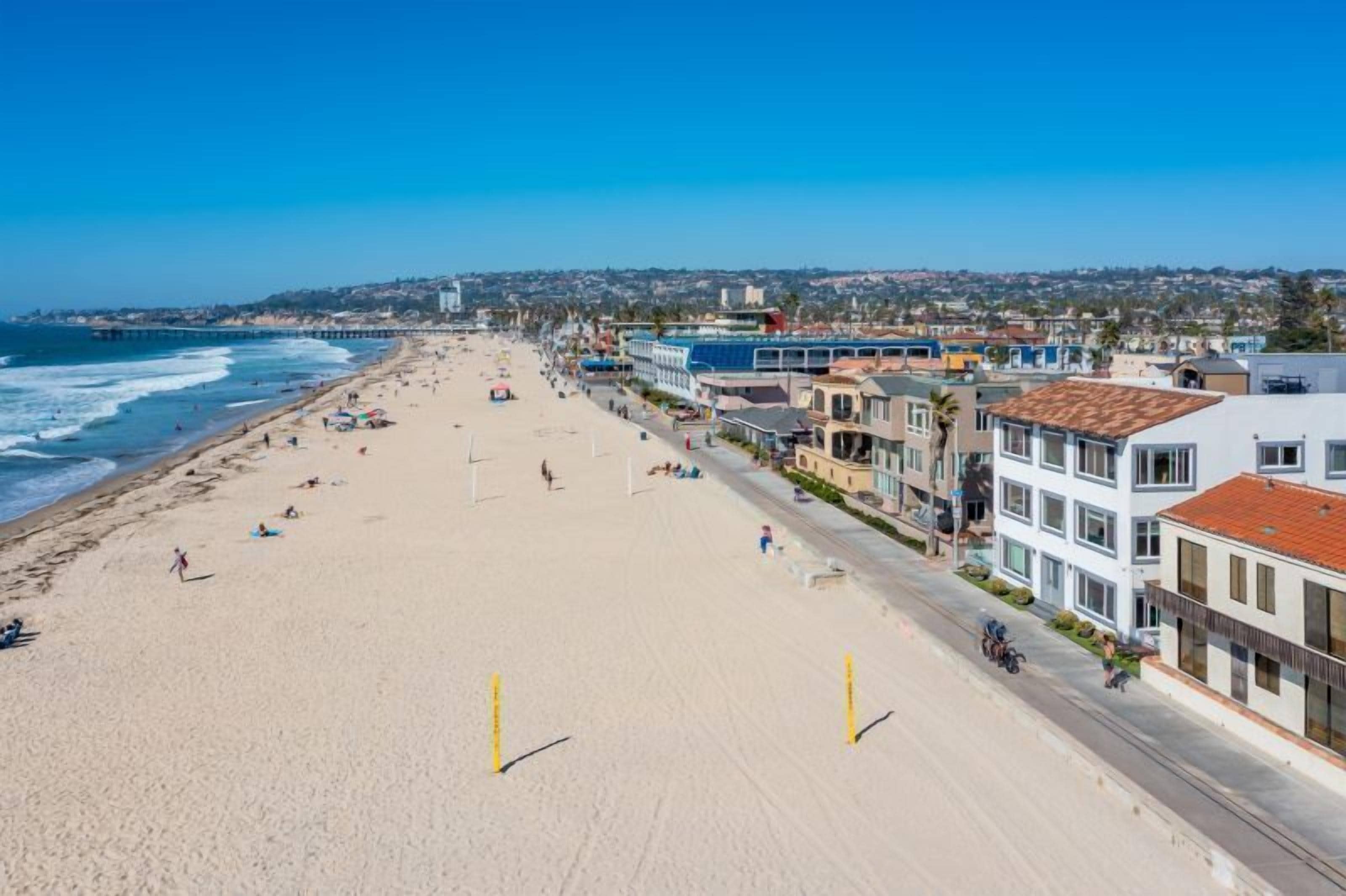 A beach with a row of buildings along the shore, a clear sky, and a view of the ocean.