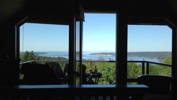 A room with a large window overlooking a scenic view of a lake and forest. - "THE LOFT" romance, luxury, stunning water and mountain views!   (Sequim)