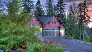 A two-story house with a red facade and a grey roof, surrounded by dense forest. - "THE LOFT" romance, luxury, stunning water and mountain views!   (Sequim)