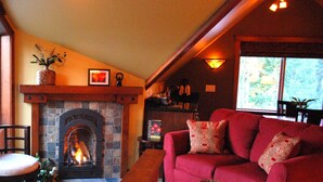 A cozy living room with a fireplace, a red sofa, and a window with a view of trees. - "THE LOFT" romance, luxury, stunning water and mountain views!   (Sequim)