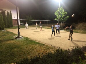 An outdoor volleyball court at night with people playing.