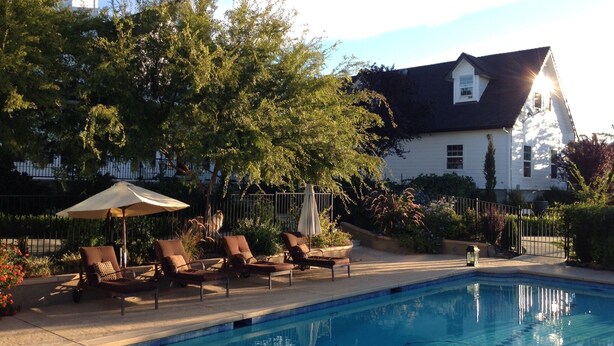 Une piscine entourée d’arbres, avec des chaises longues et des parasols, et une maison en arrière-plan.