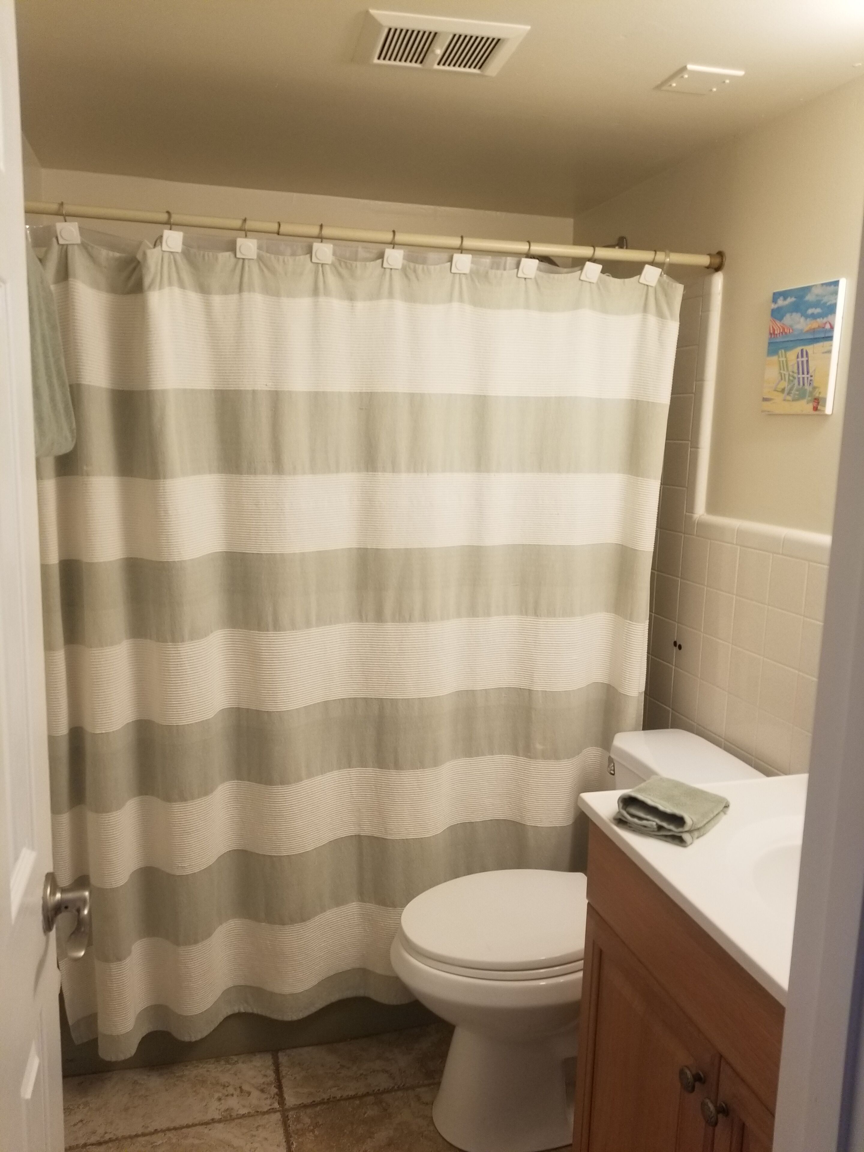 A bathroom with a striped shower curtain, a white toilet, and a wooden cabinet.