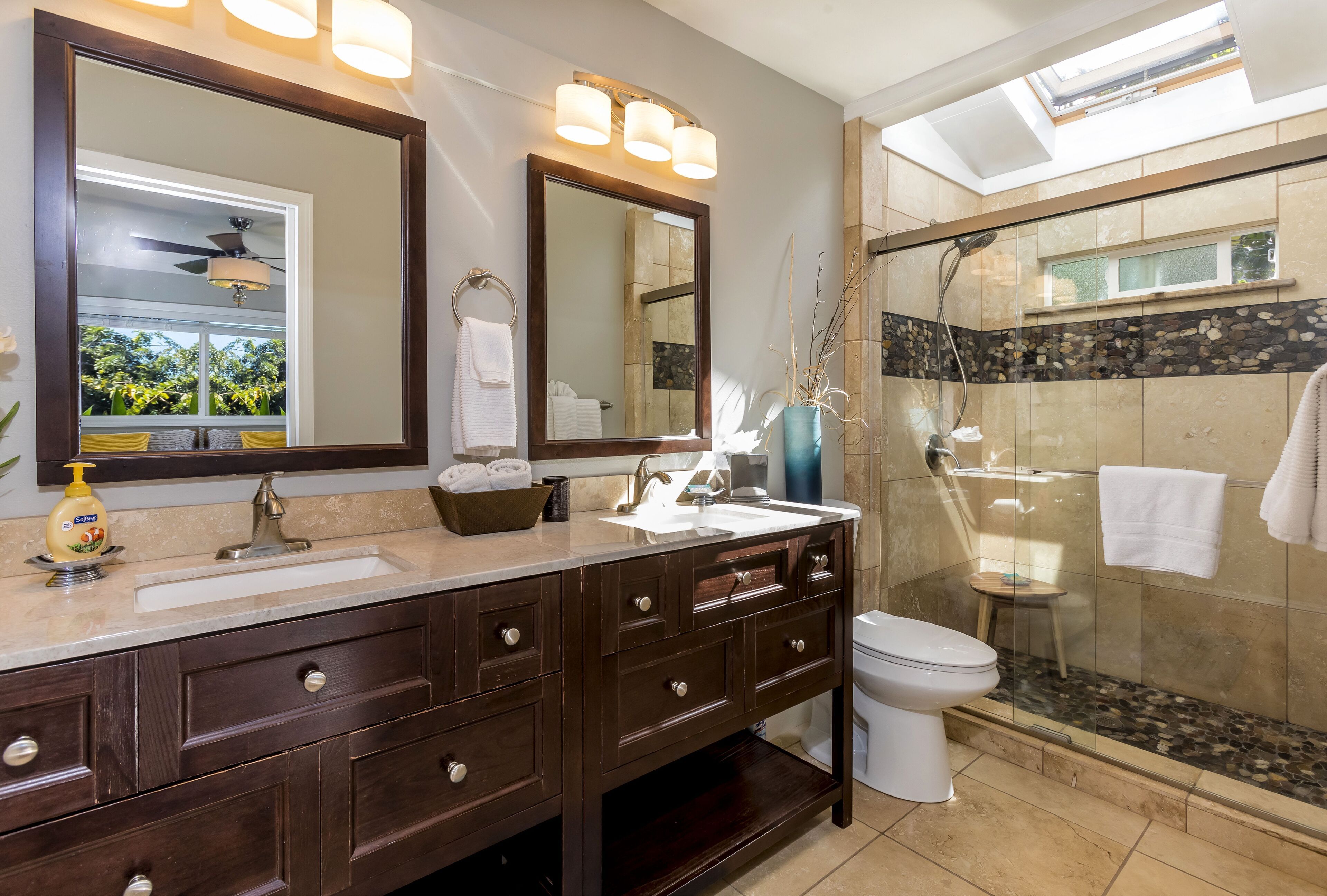 A modern bathroom with a large mirror, dual sinks, a toilet, and a glass-enclosed shower.