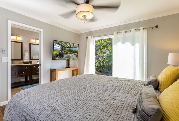 A bedroom with a large bed, a ceiling fan, a nightstand, a mirror, and a window with curtains. - CLOUD NINE BEACH HOUSE with Pool, Oceanview, Walk to Beach, Lots of Amenities (Kihei)