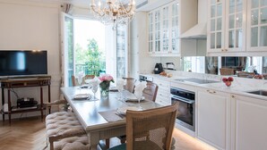 A spacious kitchen with white cabinetry, a dining area with a wooden table and chairs, and a large window providing a view of greenery outside.