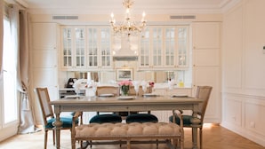 A dining area with a wooden table, cushioned chairs, and a chandelier.