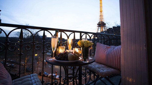 A balcony with a table set for a meal, a cushioned bench, and a view of the Eiffel Tower.