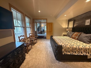 Une chambre à coucher comprenant un lit, une commode, un téléviseur et un coin salon avec des fauteuils.