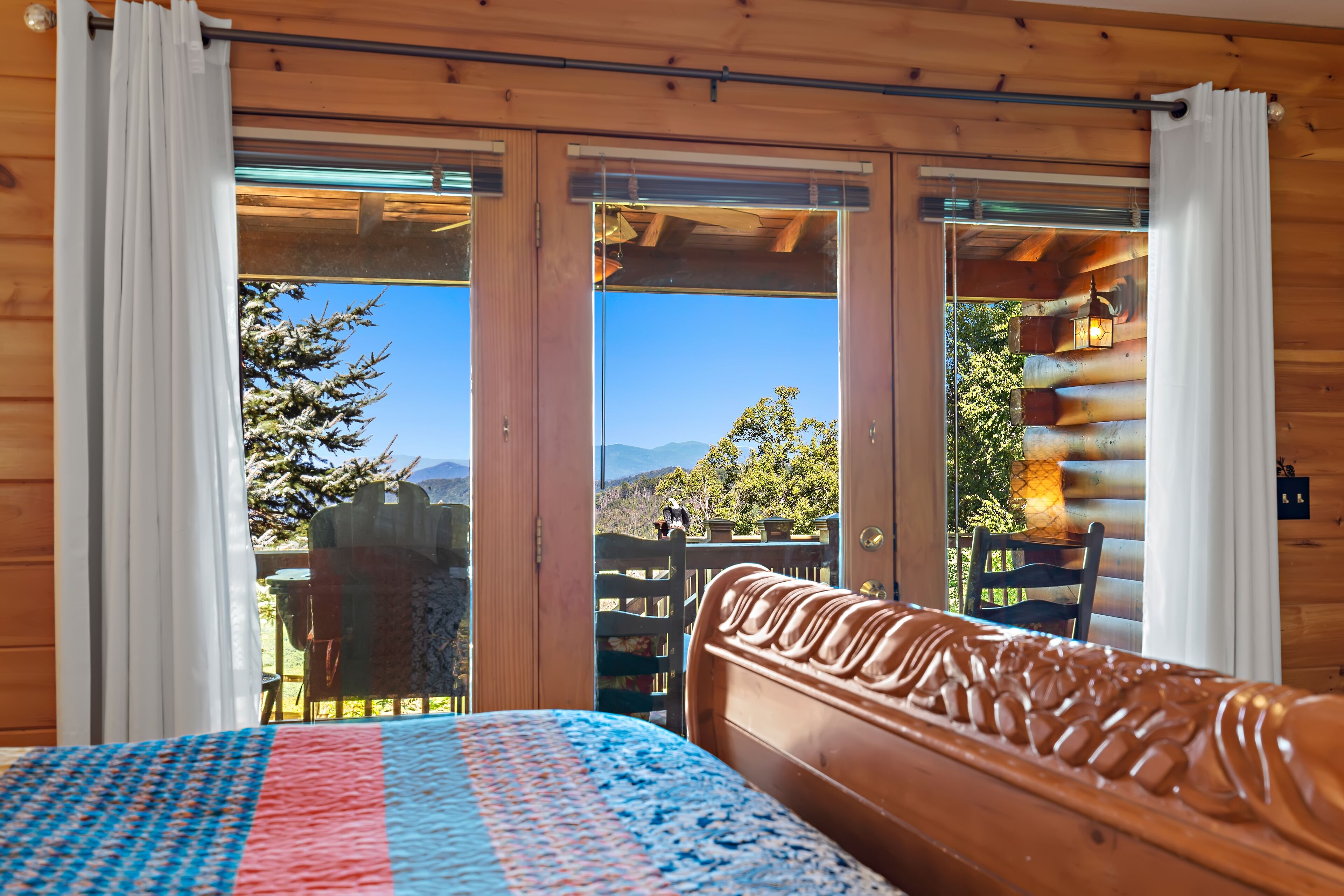 A wooden cabin room with a bed, a view of the outdoors, and a wooden headboard.