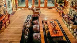 Interior espacioso de una cabaña de madera con techos altos, ventanas grandes, chimenea y un rincón de estar acogedor.