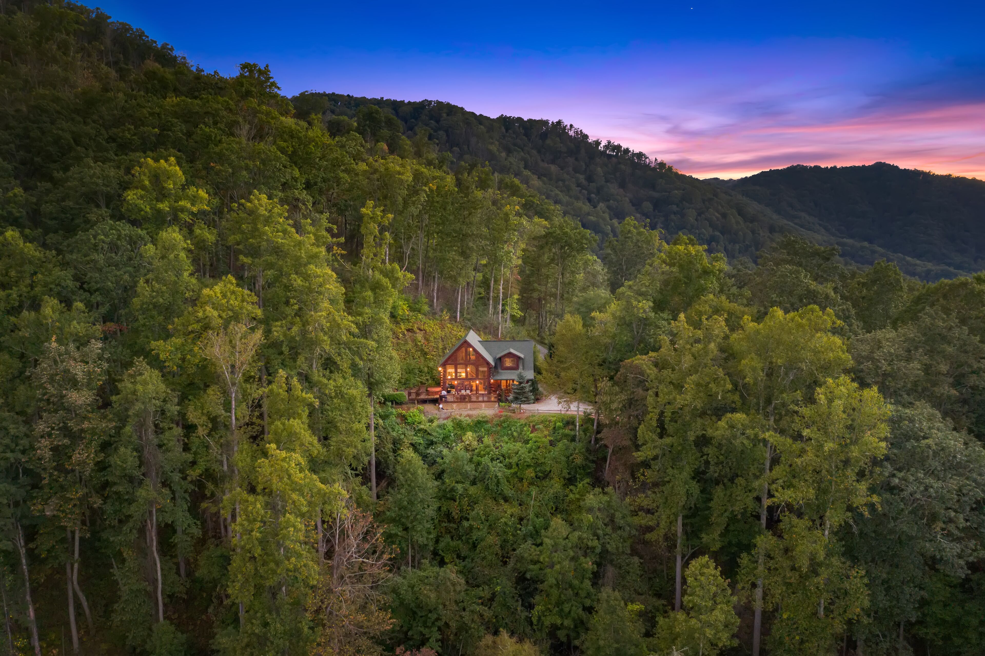 A cabin surrounded by dense forest, with a prominent wooden structure and a visible deck area.
