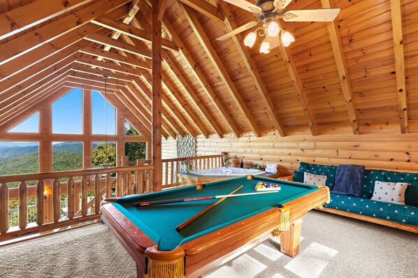 Un interior de madera con mesa de billar, sofá y balcón con vistas.