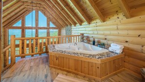 Una cabaña de troncos con interior de madera, un jacuzzi y vistas a la montaña a través de amplias ventanas.