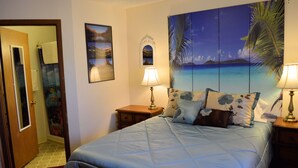 Ein Schlafzimmer mit einem Bett, zwei Nachttischen, einer Wand mit drei gerahmten Bildern und einer Tür zu einem anderen Raum.