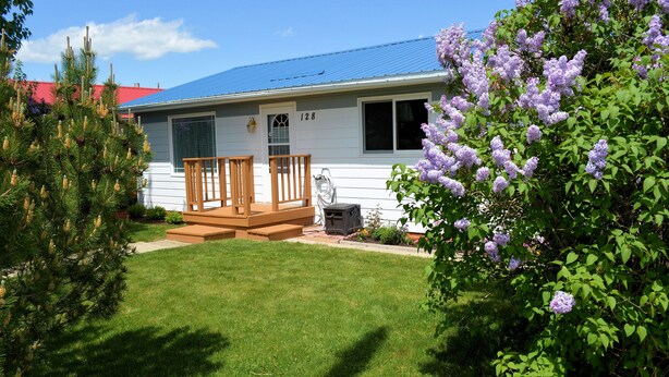 Ein eingeschossiges Haus mit blauem Dach, einer Veranda mit Holzgeländer und der Hausnummer 128.