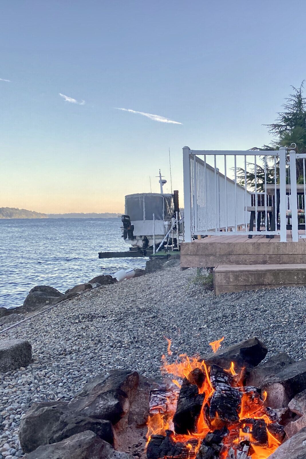 Ein Kiesstrand mit Feuerstelle, einer Überdachung und einem weißen Zaun.