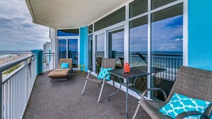 Ein Balkon mit Korbmöbeln, einem kleinen Tisch und Blick auf den Strand.