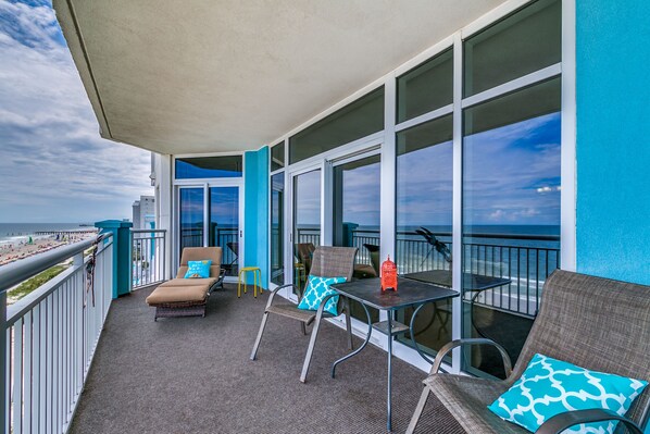 A balcony with wicker furniture, a small table, and a view of the beach.