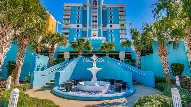 Ein Hotel mit einem Brunnen in der Mitte, umgeben von Palmen und einer blauen Fassade.